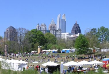 Tentes blanches et promeneurs sur la pelouse de Piedmont Park pendant le Dogwood Festival, avec les gratte-ciel de Midtown Atlanta sous un ciel bleu