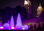 Sculptures lumineuses violettes et roses dans l'Atlanta Botanical Garden, de nuit, avec les gratte-ciel de Midtown illuminés en arrière-plan