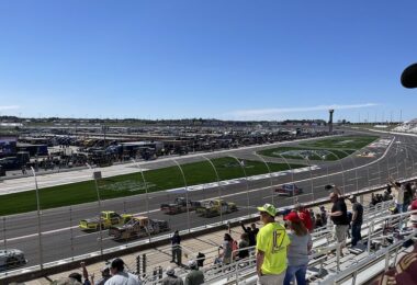 Pick-up de course NASCAR en peloton sur la ligne droite du circuit d'Atlanta, vus depuis les tribunes où se tiennent quelques spectateurs