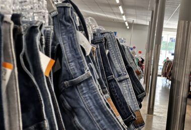 Gros plan sur une longue rangée de jeans d'occasion suspendus à des cintres transparents, avec leurs étiquettes de prix, dans l'allée d'une grande friperie aux néons