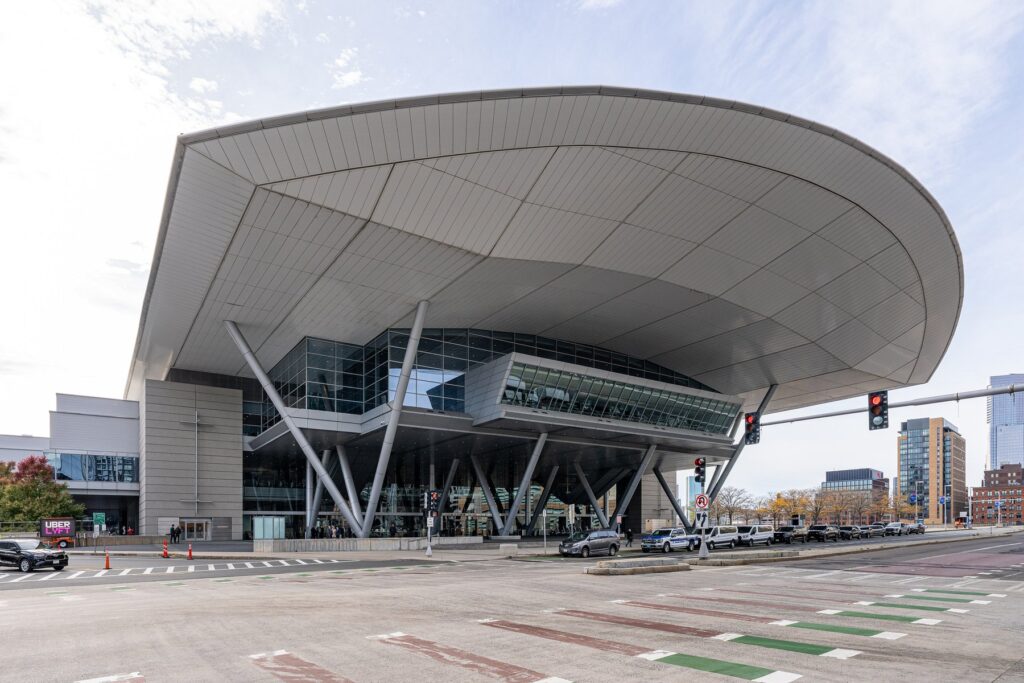 Façade du centre des congrès de Boston, avec son immense toit incurvé porté par des piliers obliques au-dessus d'une entrée vitrée, vue depuis un carrefour de Summer Street