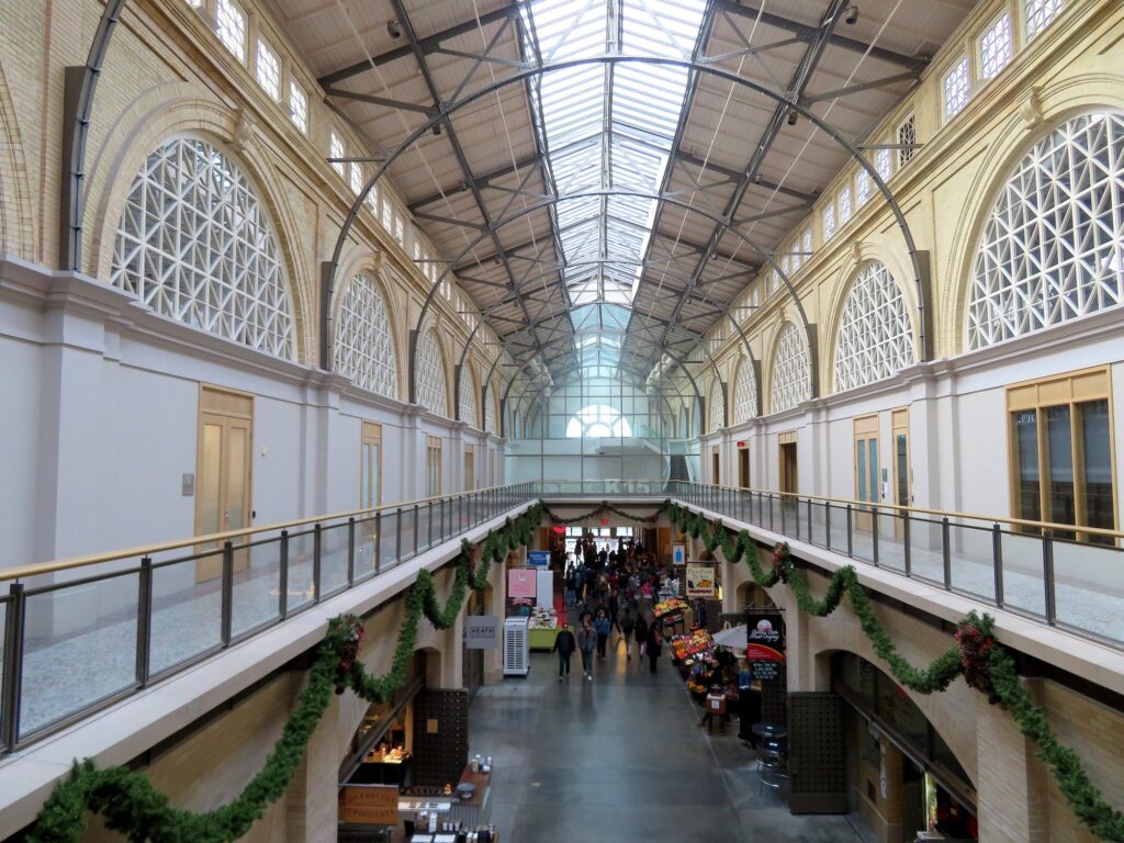 Intérieur du Ferry Building vu depuis la galerie de l'étage : longue nef sous une verrière à charpente métallique, fenêtres en demi-cercle, commerces au rez-de-chaussée