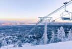 Télésiège couvert de givre au-dessus d'une piste damée de Bear Mountain, avec la forêt enneigée et la vallée de Big Bear Lake au lever du jour