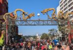 Foule massée sous le portique de Chinatown, une arche métallique surmontée de deux grands dragons dorés, avec des bannières jaunes de danse du lion au premier plan