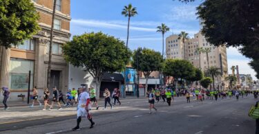 Des dizaines de coureurs, beaucoup en tee-shirts jaune fluo, remontent Hollywood Boulevard sous un ciel bleu, entre palmiers et immeubles anciens, avec au loin l'enseigne verticale du théâtre Pantages