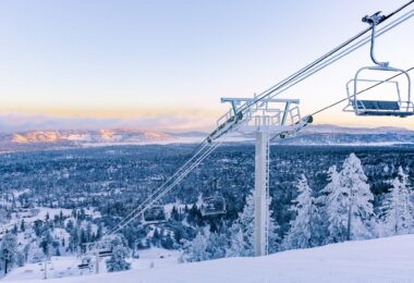 Télésiège couvert de givre au-dessus d'une piste damée de Bear Mountain, avec la forêt enneigée et la vallée de Big Bear Lake au lever du jour