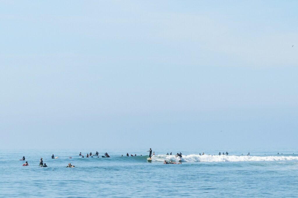 Longboardeur debout sur une petite vague de Malibu, entouré d'une cinquantaine de surfeurs qui attendent leur tour sur leur planche