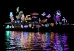 Bateau couvert de guirlandes lumineuses multicolores dessinant des personnages, de nuit, avec ses reflets dans l'eau du port de Newport Beach