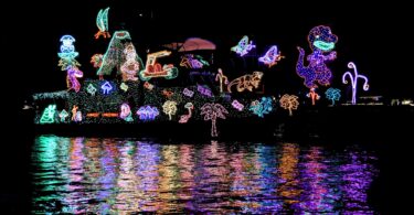Bateau couvert de guirlandes lumineuses multicolores dessinant des personnages, de nuit, avec ses reflets dans l'eau du port de Newport Beach