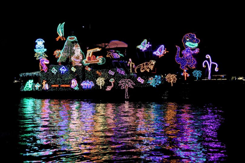 Bateau couvert de guirlandes lumineuses multicolores dessinant des personnages, de nuit, avec ses reflets dans l'eau du port de Newport Beach