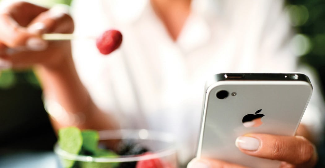 Woman eating fruits dessert with iPhone 4s in hands