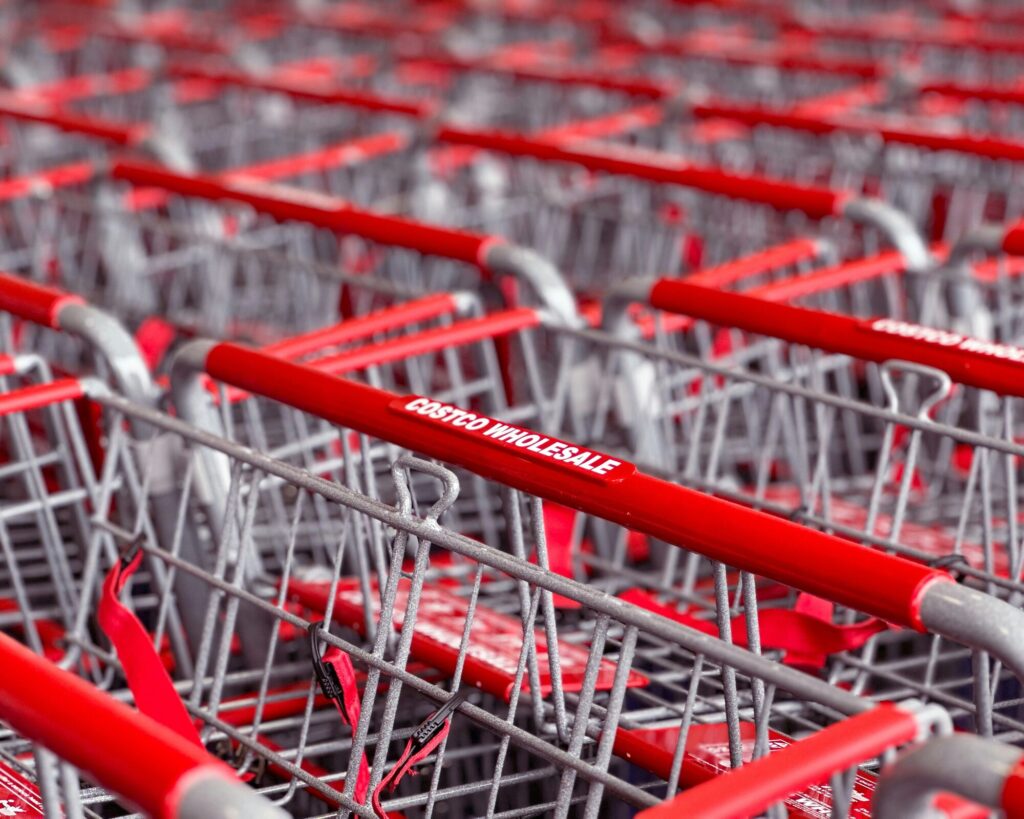 Gros plan sur des rangées de caddies métalliques aux poignées rouges marquées « Costco Wholesale »