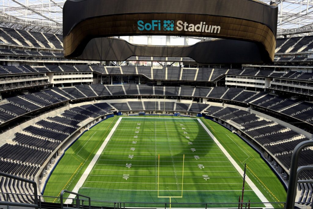 Intérieur du SoFi Stadium vide, terrain de football américain vu des gradins supérieurs, sous l'anneau d'écran géant et la toiture translucide