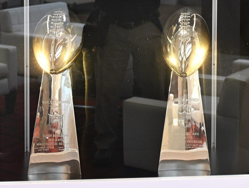 Deux trophées Vince Lombardi en argent, un ballon de football américain sur une base gravée du logo NFL, exposés dans une vitrine