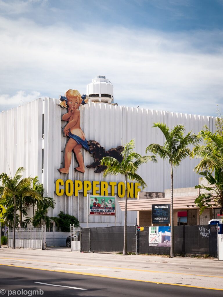 L'enseigne historique Coppertone sur la façade d'un immeuble de Biscayne Boulevard : une fillette blonde dont un petit chien tire le maillot, au-dessus du mot COPPERTONE en lettres jaunes, entre des palmiers