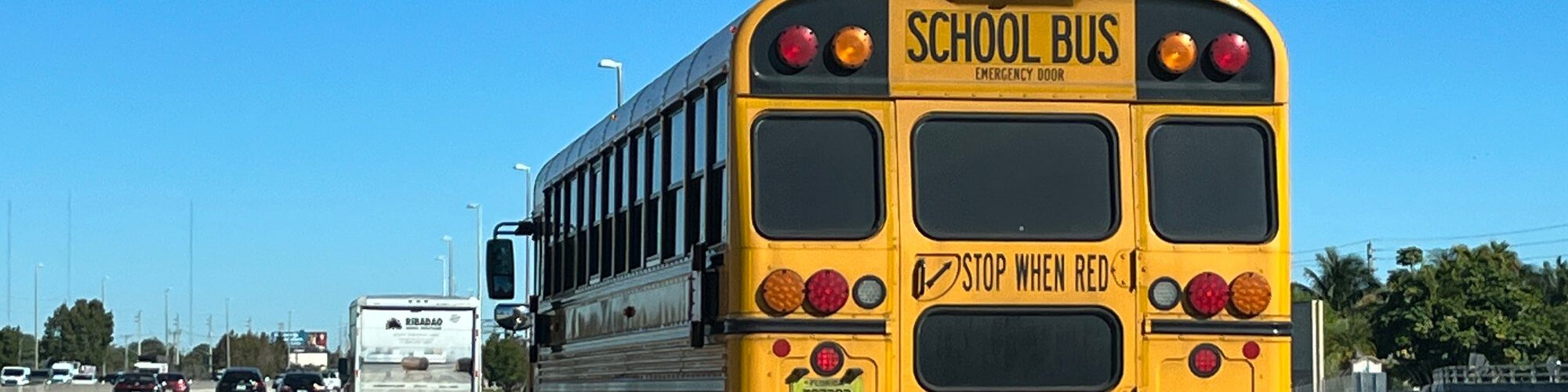 Bus scolaire jaune vu de l'arrière, avec l'inscription School Bus et Stop when red lights flash, sur une autoroute de Floride sous un ciel bleu
