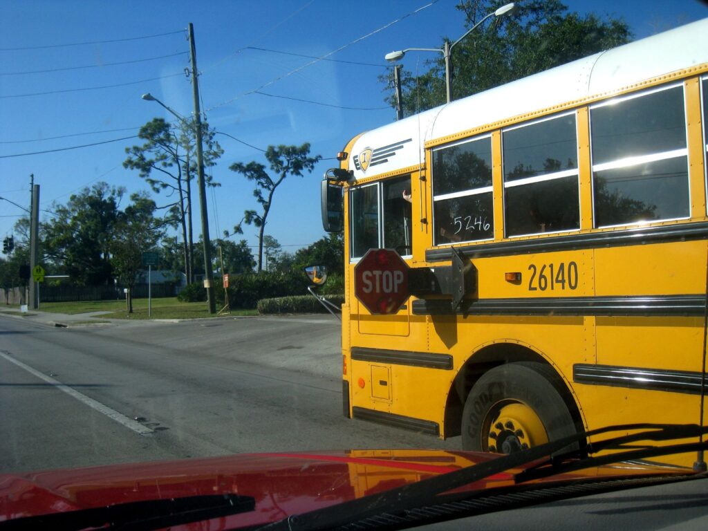 Bus scolaire jaune vu depuis une voiture, son panneau STOP rouge déployé sur le côté, au bord d'une route d'Orlando