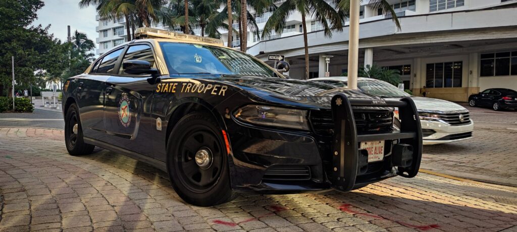 Dodge Charger noire et beige de la Florida Highway Patrol, marquée State Trooper, garée sur un trottoir pavé de Miami Beach devant des palmiers
