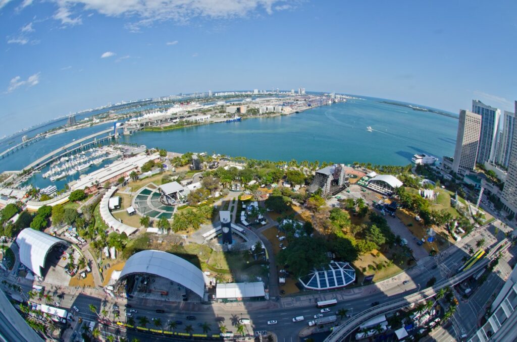 Vue aérienne en grand angle de Bayfront Park au bord de la baie de Biscayne, avec les scènes et chapiteaux blancs d'un festival installés entre les arbres, la marina à gauche et le port de Miami à l'horizon