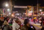 Main Street à Daytona Beach la nuit, sous une banderole Welcome to Daytona Beach Bike Week, avec des motos feux allumés au milieu d'une foule de motards et de badauds