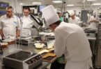 Un candidat en toque travaille une préparation pendant l’épreuve de pâtisserie du concours Meilleur Ouvrier de France, observé par des membres du jury