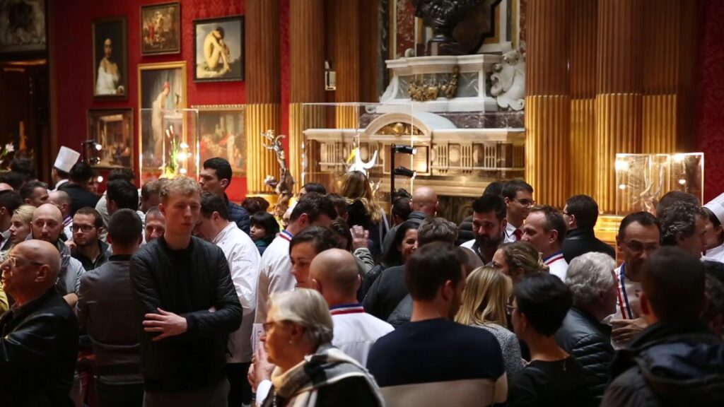Foule de visiteurs et de chefs, dont plusieurs portent le col bleu-blanc-rouge, lors de la présentation des pièces du concours Meilleur Ouvrier de France pâtisserie