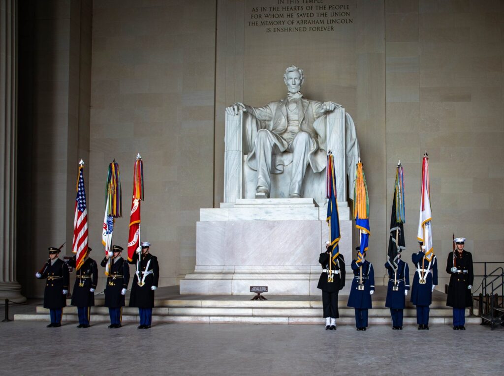 La statue d'Abraham Lincoln assis dans le Lincoln Memorial, avec à ses pieds une garde d'honneur des différentes armées portant leurs drapeaux