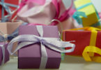 Petites boîtes cadeaux en papier violet, rouge, rose et jaune, nouées de rubans de satin, avec au premier plan une boîte violette au ruban blanc