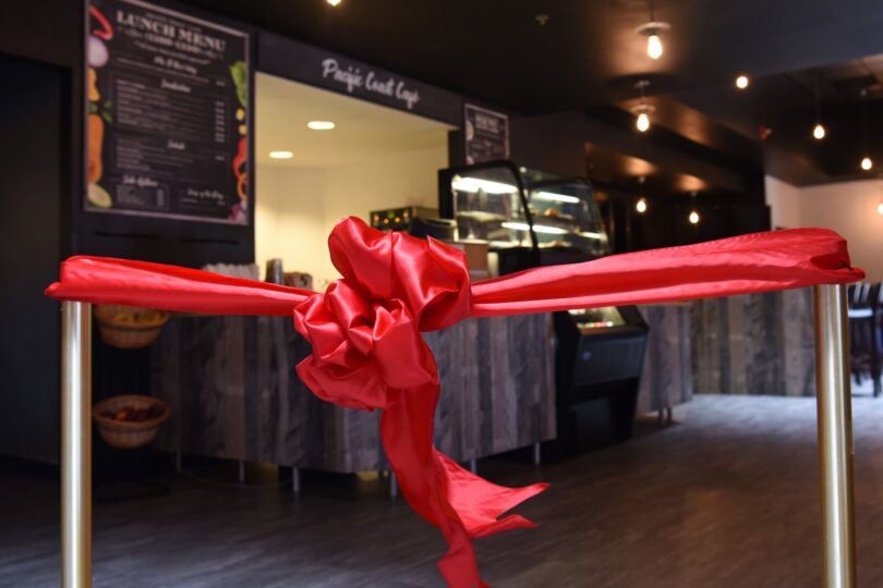 Ruban de satin rouge noué entre deux poteaux dorés devant le comptoir et la vitrine d’un café, juste avant son inauguration