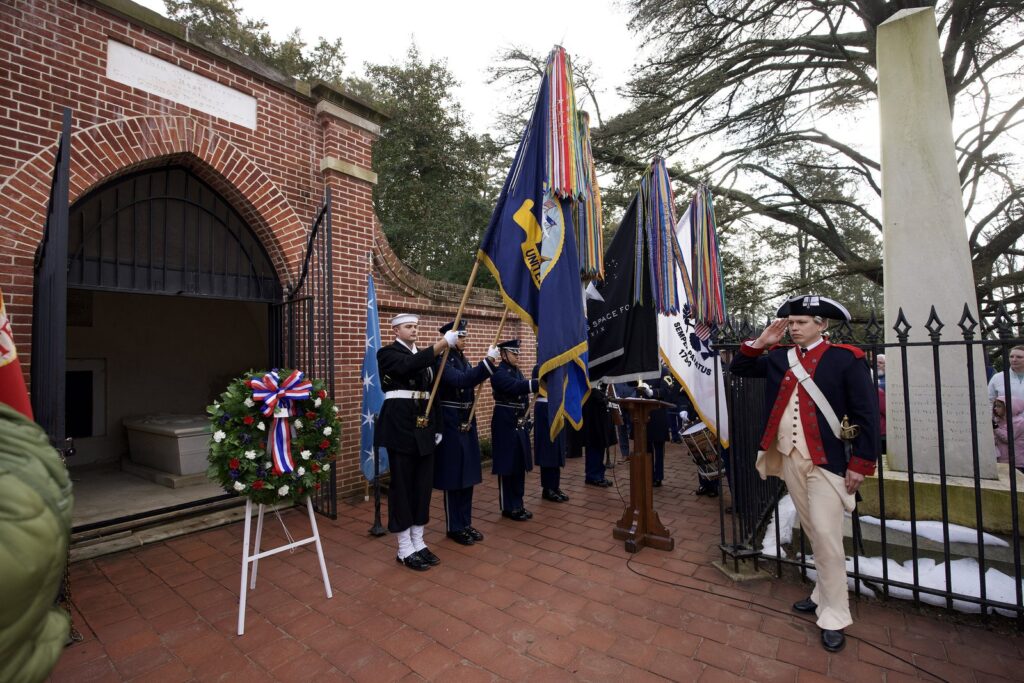 Une gerbe tricolore posée devant l'entrée voûtée en brique du tombeau de George Washington, entre une garde au drapeau et un soldat en uniforme de l'armée continentale qui salue