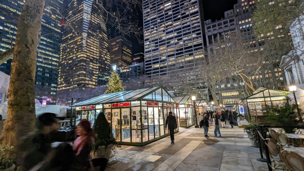 Chalets de verre éclairés la nuit dans un parc, un sapin de Noël illuminé et des gratte-ciel allumés en arrière-plan