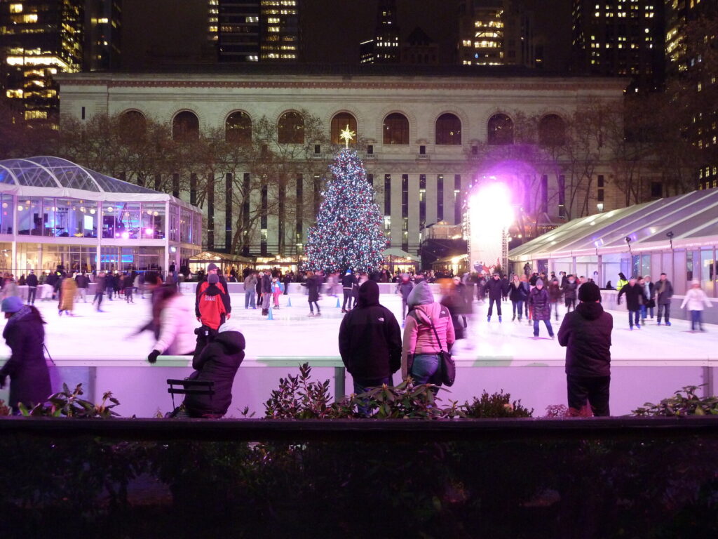 Patinoire extérieure éclairée en violet la nuit, avec un grand sapin de Noël illuminé et la façade d'un bâtiment classique en arrière-plan