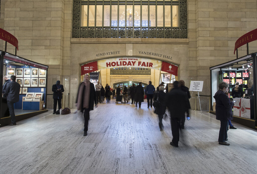Hall monumental d'une gare avec une bannière rouge « Grand Central Holiday Fair » au-dessus de l'entrée et des stands de marché de chaque côté