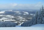 Piste enneigée bordée de sapins givrés au sommet d'Elk Mountain, avec en contrebas le pied des pistes et une vallée de champs enneigés et de forêts du nord-est de la Pennsylvanie