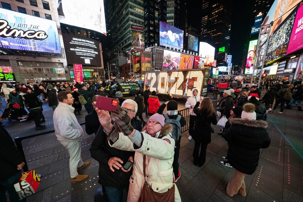Des passants se prennent en photo devant les grands chiffres lumineux 2023 exposés sur une place de Times Square, de nuit
