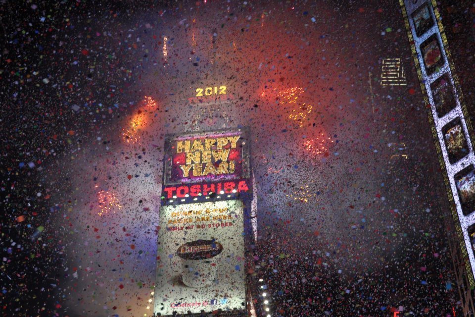 One Times Square de nuit sous une pluie de confettis et de feux d'artifice, avec l'inscription Happy New Year