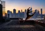 Silhouette à contre-jour d'une danseuse en plein saut sur le toit d'un immeuble, devant les gratte-ciel de Manhattan au crépuscule
