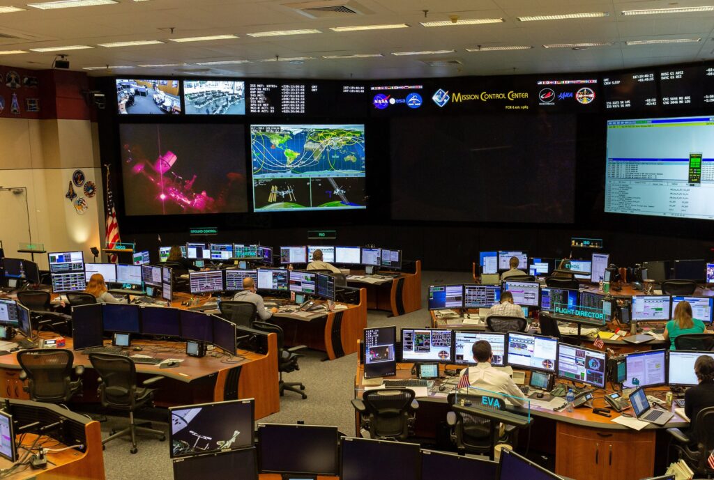 Contrôleurs devant leurs consoles et les écrans muraux de la salle de contrôle des vols du Johnson Space Center