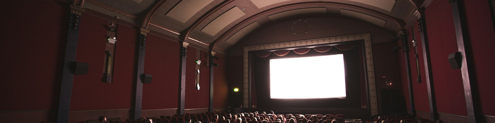 Public dans une salle de cinéma aux fauteuils rouges, face à l'écran allumé