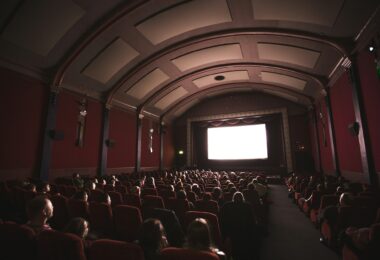 Public dans une salle de cinéma aux fauteuils rouges, face à l'écran allumé