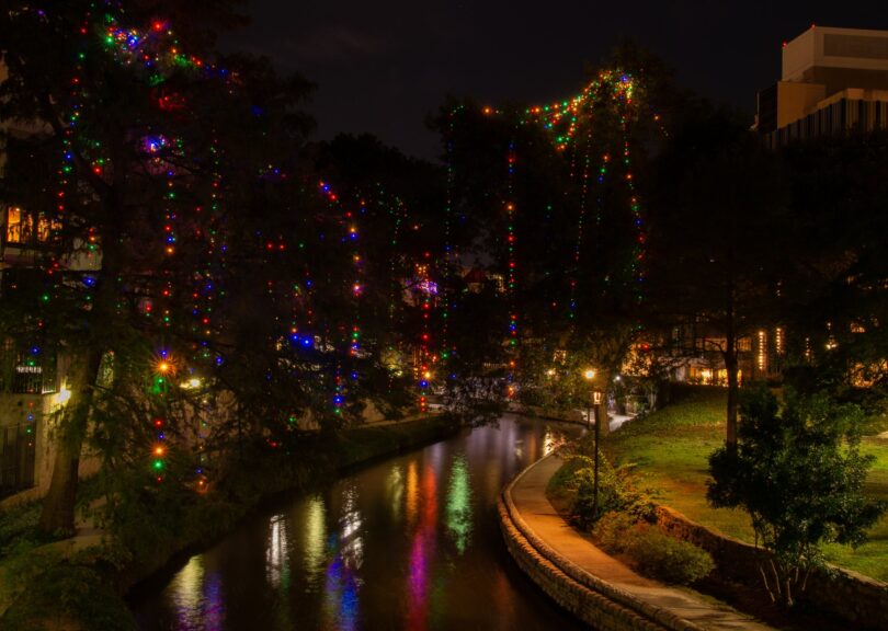 Cyprès du River Walk de San Antonio couverts de guirlandes lumineuses multicolores, de nuit, avec leurs reflets dans la rivière
