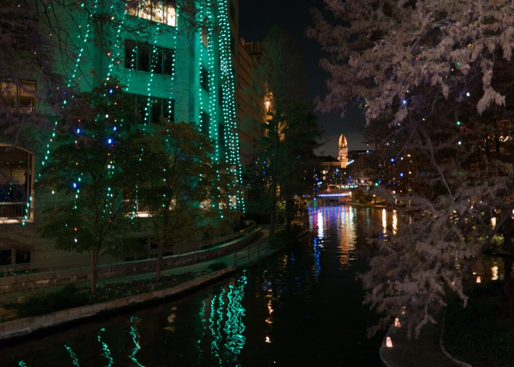 Le River Walk de San Antonio la nuit, avec des façades et des arbres illuminés de vert et de blanc qui se reflètent dans l'eau