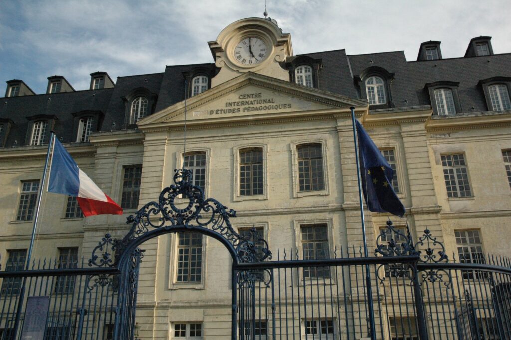 Façade classique à horloge de France Éducation international, ancien CIEP, à Sèvres, derrière sa grille, avec les drapeaux français et européen