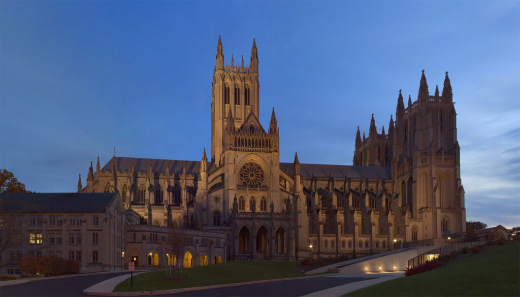Cathédrale gothique en pierre claire illuminée au crépuscule sous un ciel bleu nuit, vue depuis sa pelouse