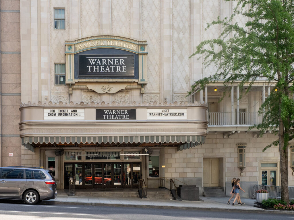 Façade de théâtre avec une marquise Art déco portant l'enseigne « Warner Theatre », vue de jour depuis la rue