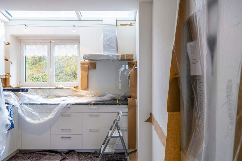 Cuisine en chantier, meubles blancs et hotte protégés par du film plastique et du papier kraft, escabeau au milieu de la pièce