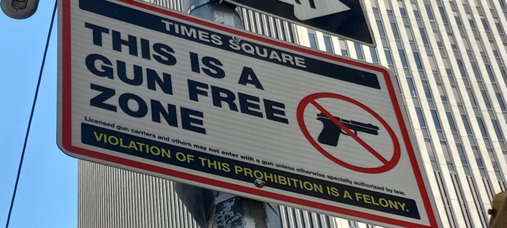 Panneau « Times Square, This is a gun free zone, violation of this prohibition is a felony » fixé à un poteau