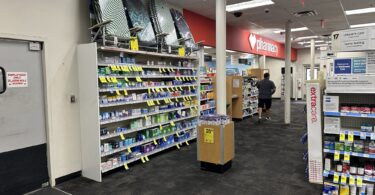 Allée d'un CVS bordée de rayons de médicaments en vente libre, avec l'enseigne rouge de la pharmacie au fond