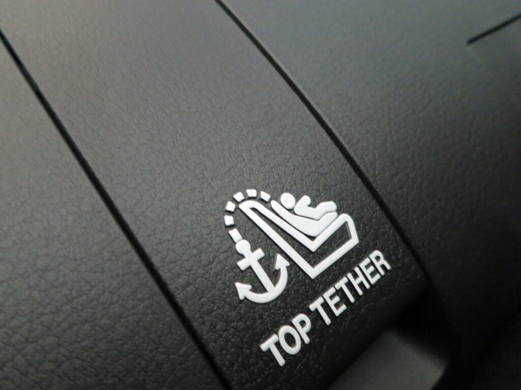 Plage arrière d'une voiture, en similicuir noir, marquée du pictogramme d'ancrage (une ancre et un siège enfant) et des mots Top Tether