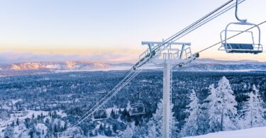 Télésiège couvert de givre au-dessus d'une piste damée de Bear Mountain, avec la forêt enneigée et la vallée de Big Bear Lake au lever du jour